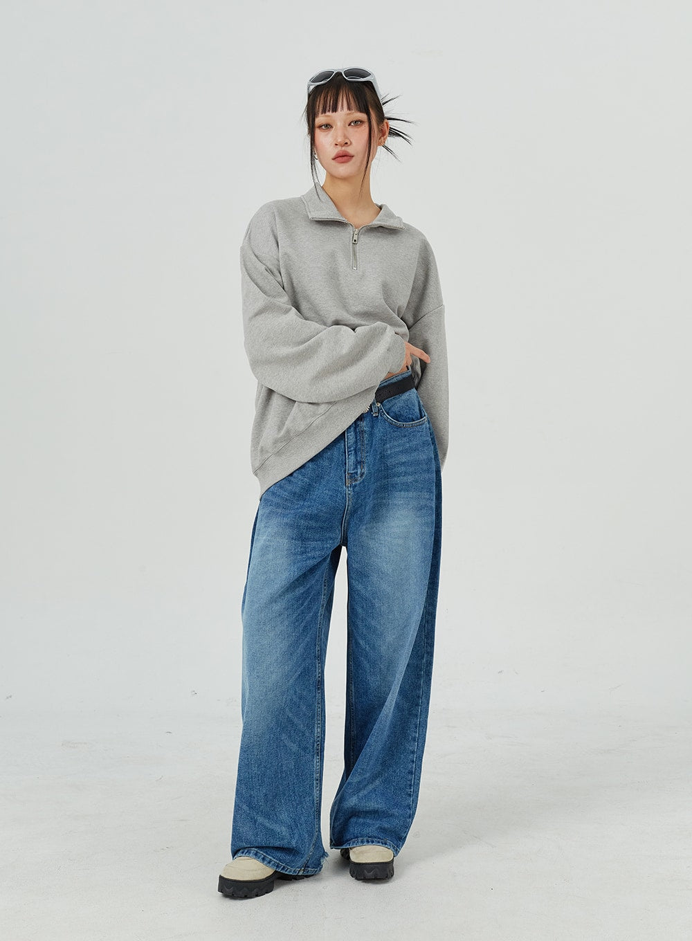 Oversized Jeans Unisex CM321 in blue, three-quarter front on model with arm crossed, wide-leg faded denim showing relaxed unisex silhouette and belt detail.