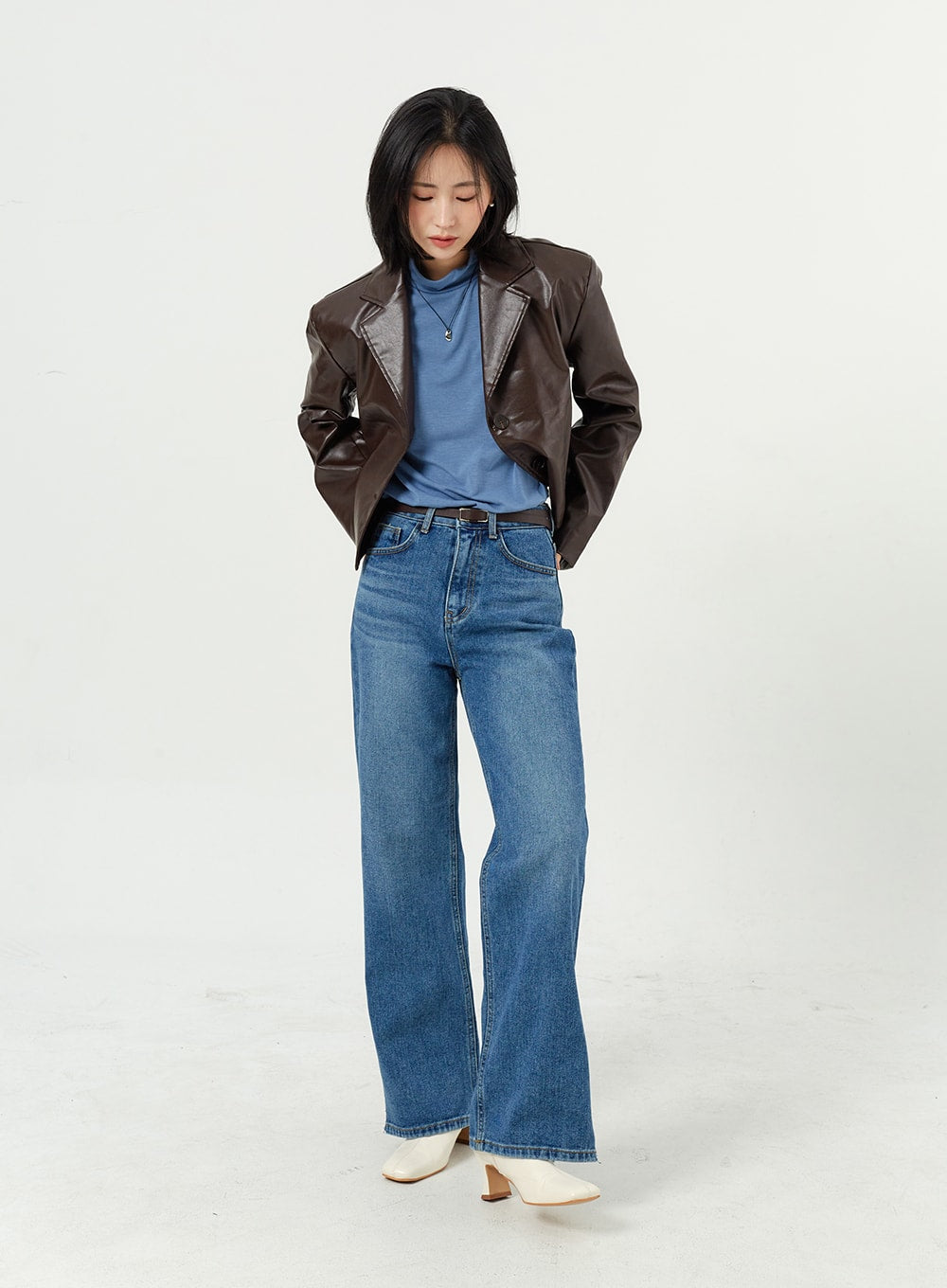 Side Slit Jeans OM308 in mid blue, full-length front shot on model looking down, wide-leg cotton denim, layered with brown leather jacket and blue tee, white boots.