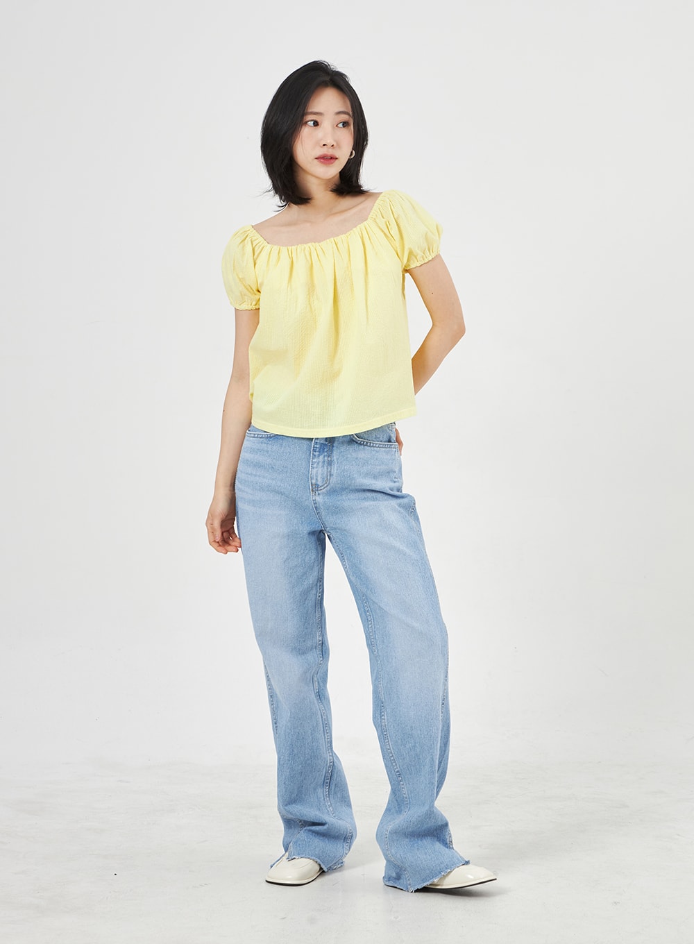 Light Wash Jeans OA310 in light blue, front three-quarter shot on model with relaxed pose, wide-fit washed denim with visible side slit at ankle, worn with yellow puff top.