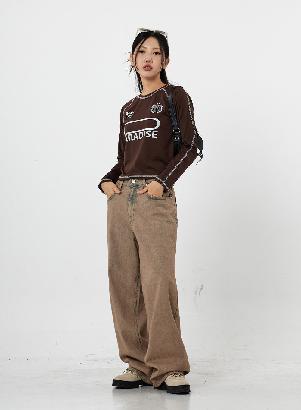 Raemon Wide Jeans Unisex CS21 in brown acid-wash, full-length three-quarter side view on model, hands in pockets, wide-leg silhouette with relaxed drape, worn with brown graphic crop top.
