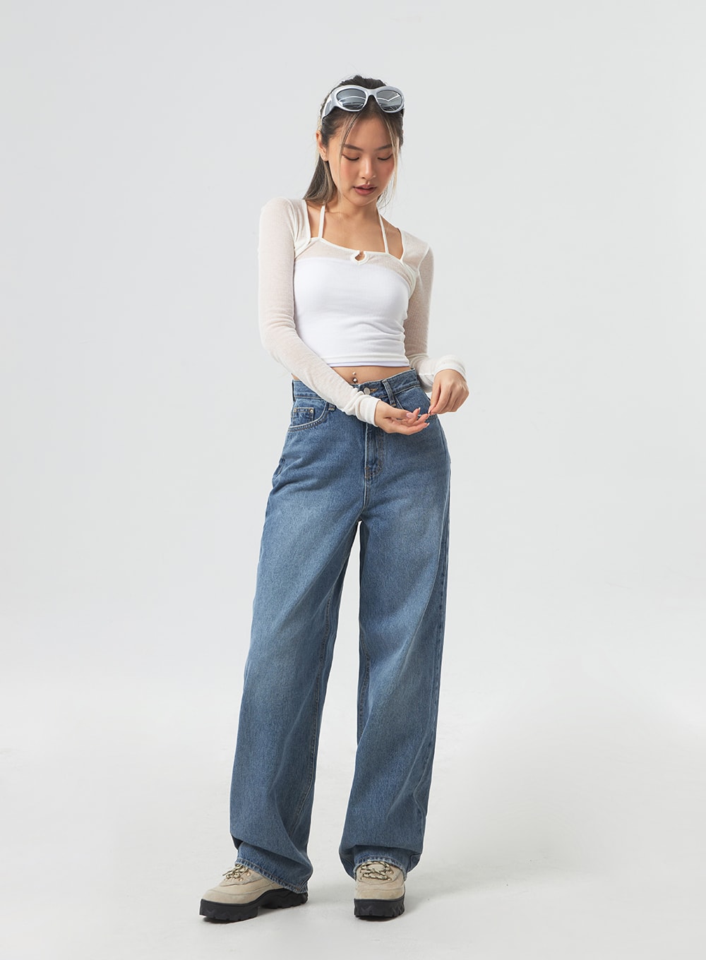 Wide Leg Mid-Wash Jeans CM331 in mid-wash blue, full-length front view on model looking down, relaxed wide-leg cotton denim, high-rise waist, styled with white mesh crop top and chunky sneakers.