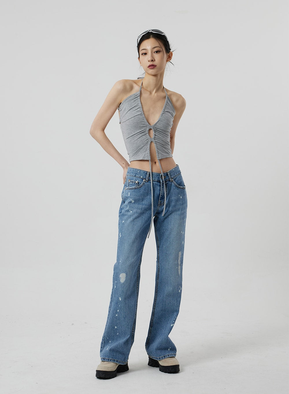 Low Rise Bootcut Jeans CF309 in blue denim, full-length front view on model, arms relaxed at sides, paint-splatter and distressing across slim bootcut leg, styled with grey ruched halter top and platform sneakers.