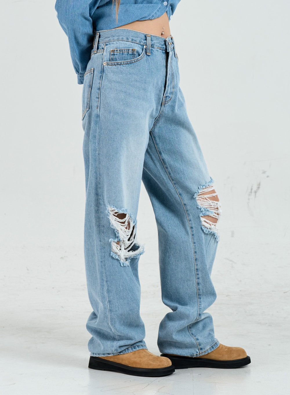 Ripped Maxi Denim Pants Unisex CO14 in light blue, side close-up on model, wide-leg cotton denim highlighting deep frayed rip details at both knees from a side angle.