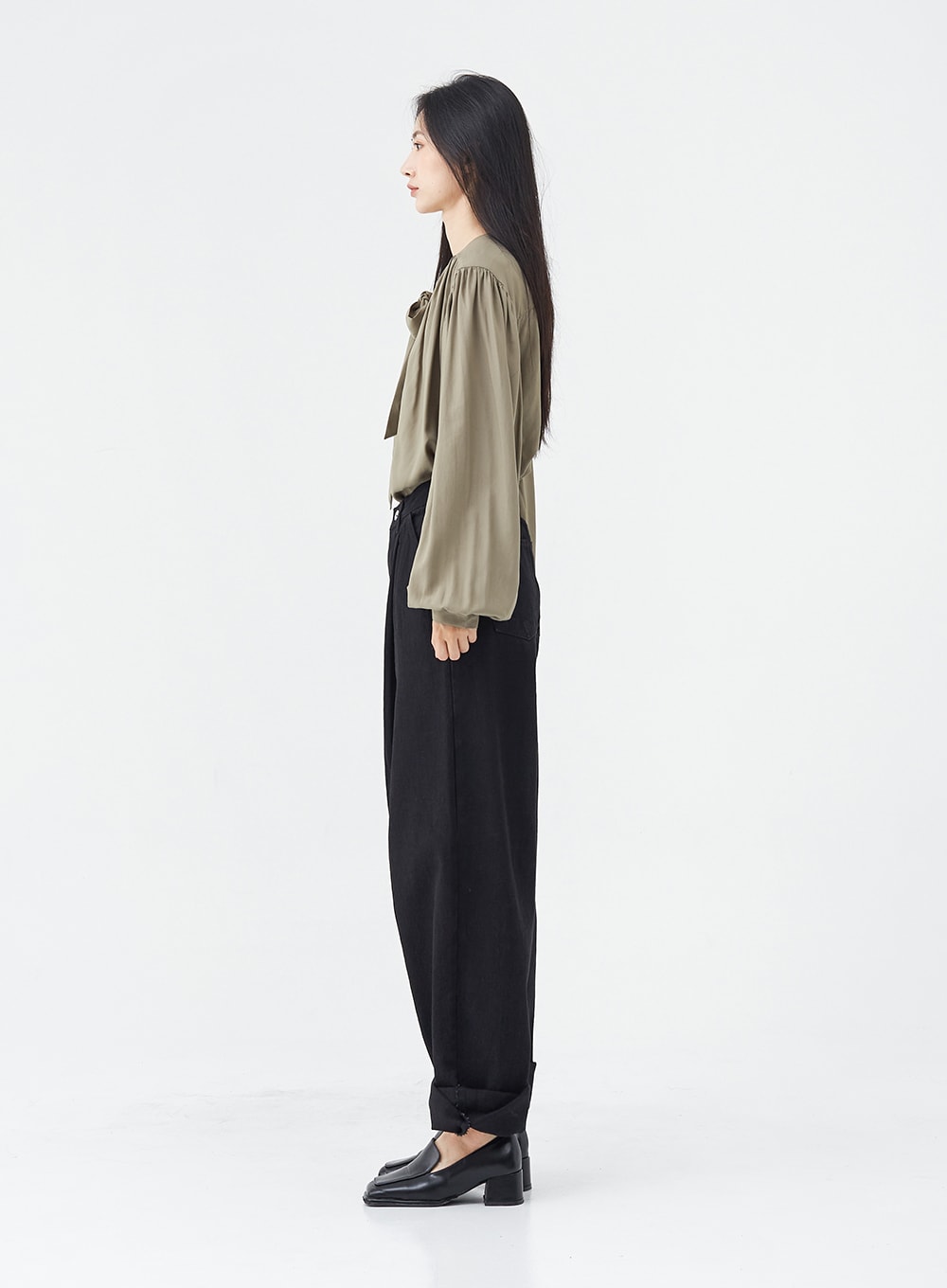 Pintuck Black Jeans OG18 in black, full side profile on model, wide-fit cotton pintuck jeans showing tapered silhouette and rolled hem, styled with olive bow blouse and loafers.