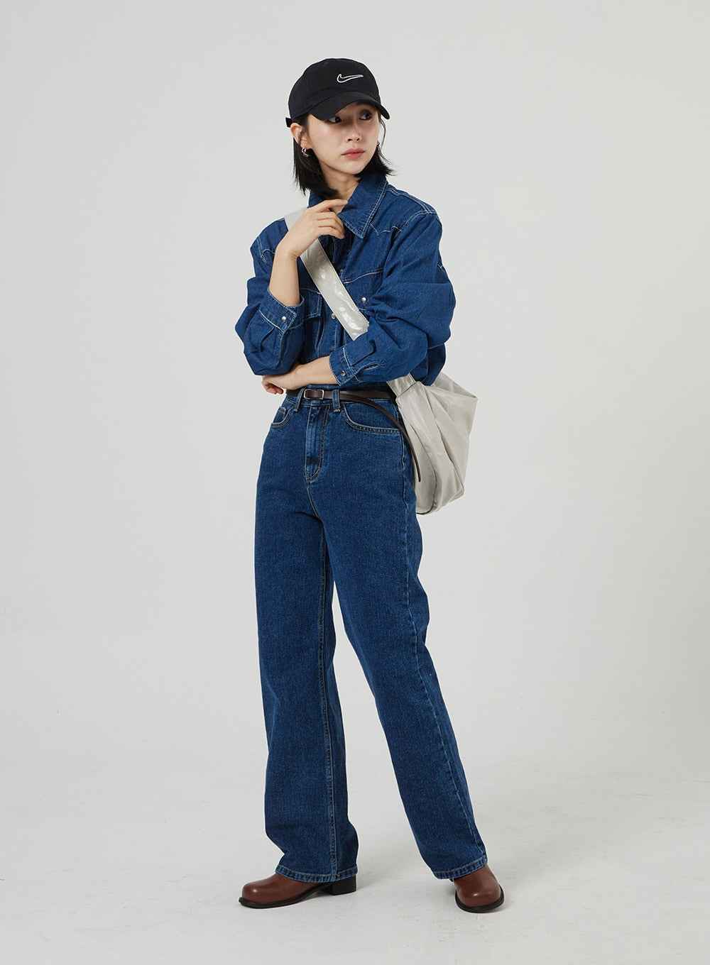 Basic Indigo Jeans OF310 in indigo, full-length front on model holding tote strap, wide-leg high-rise denim with brown belt, paired with denim shirt, black cap, and brown leather boots.