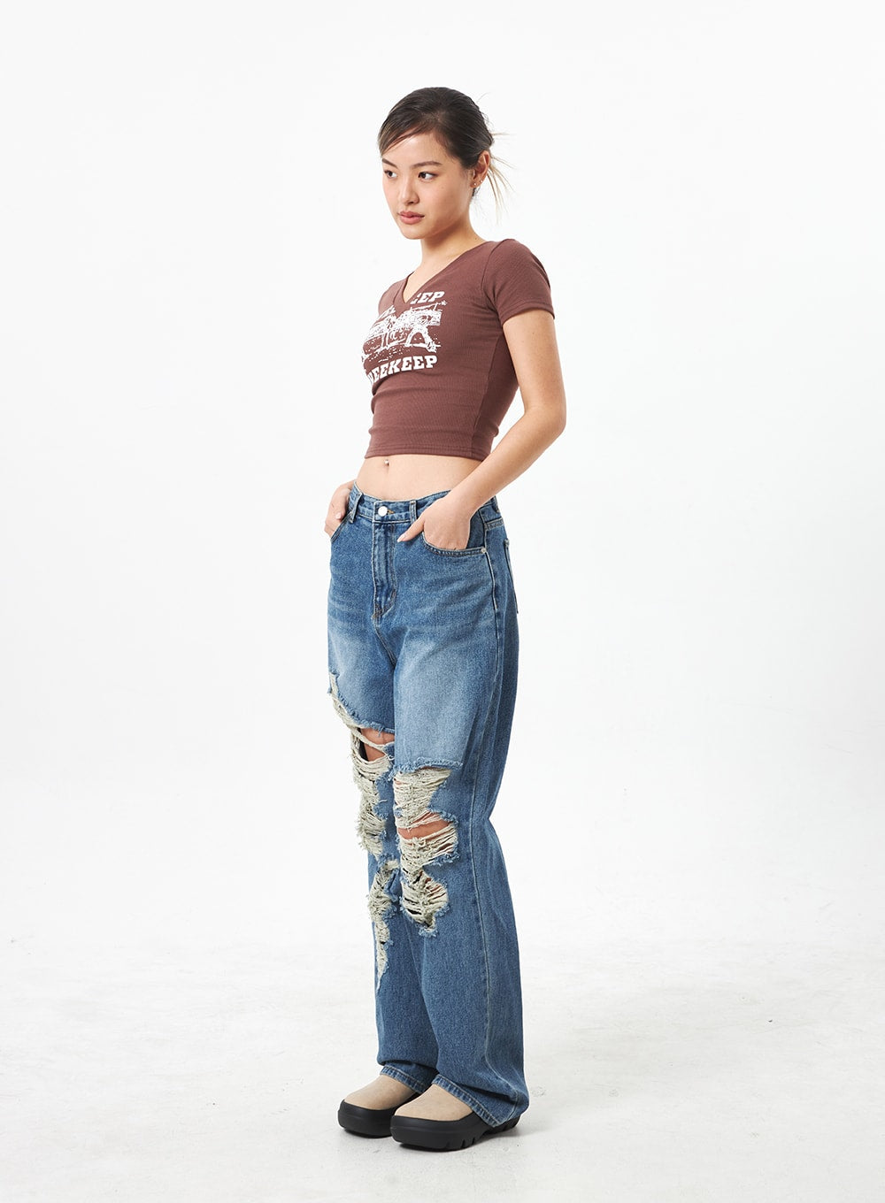 Wide Ripped Jeans CA304 in medium blue, side-angle full-body view on model, showing profile of wide-leg silhouette, deep knee rips with dangling frayed threads, paired with brown crop tee.