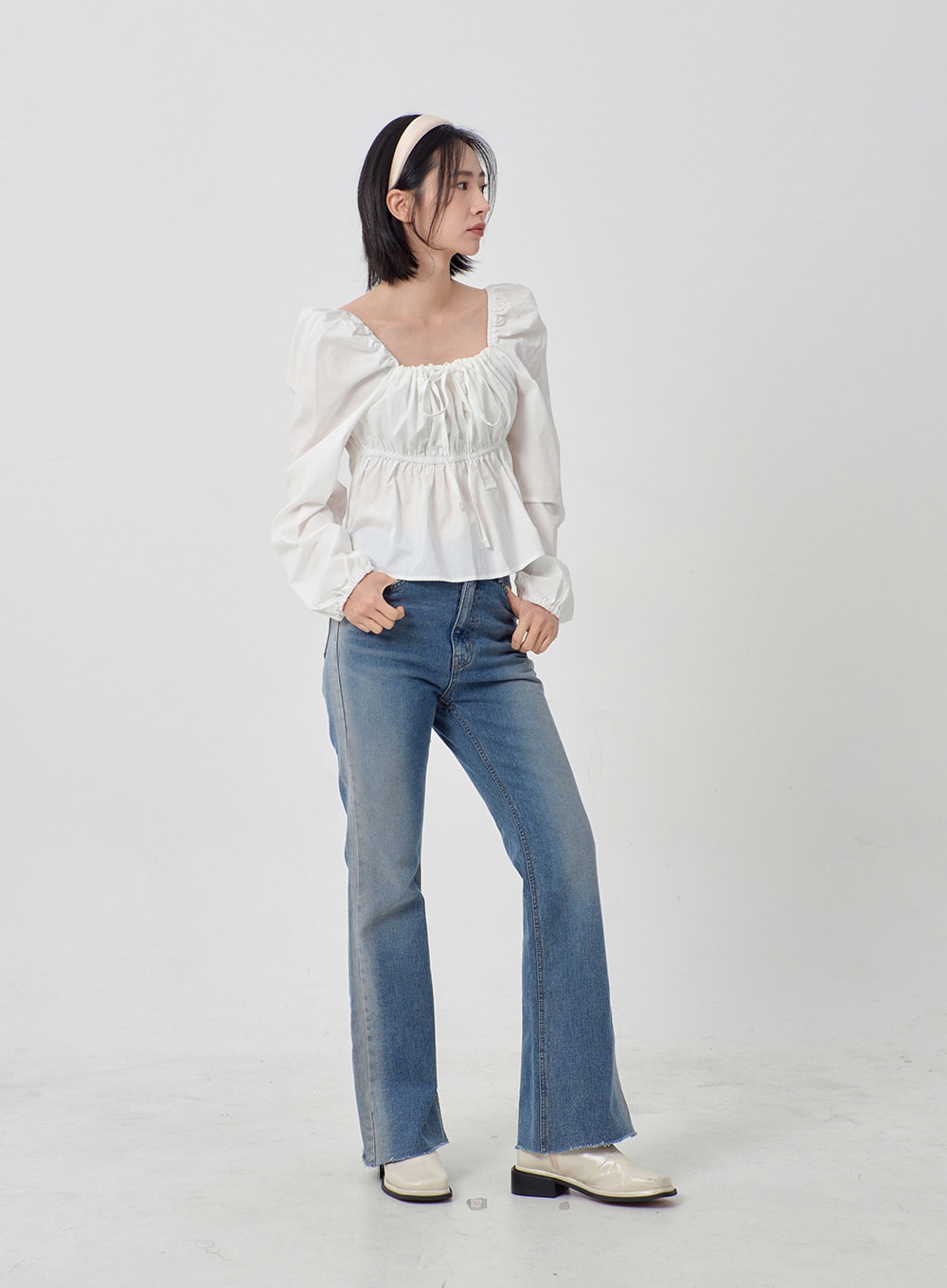 Light Washed Bootcut Jeans OD27 in light blue, angled full-length view on model, slim-fit washed cotton bootcut denim, raw frayed hem at ankle, paired with white ruffle blouse and cream loafers.