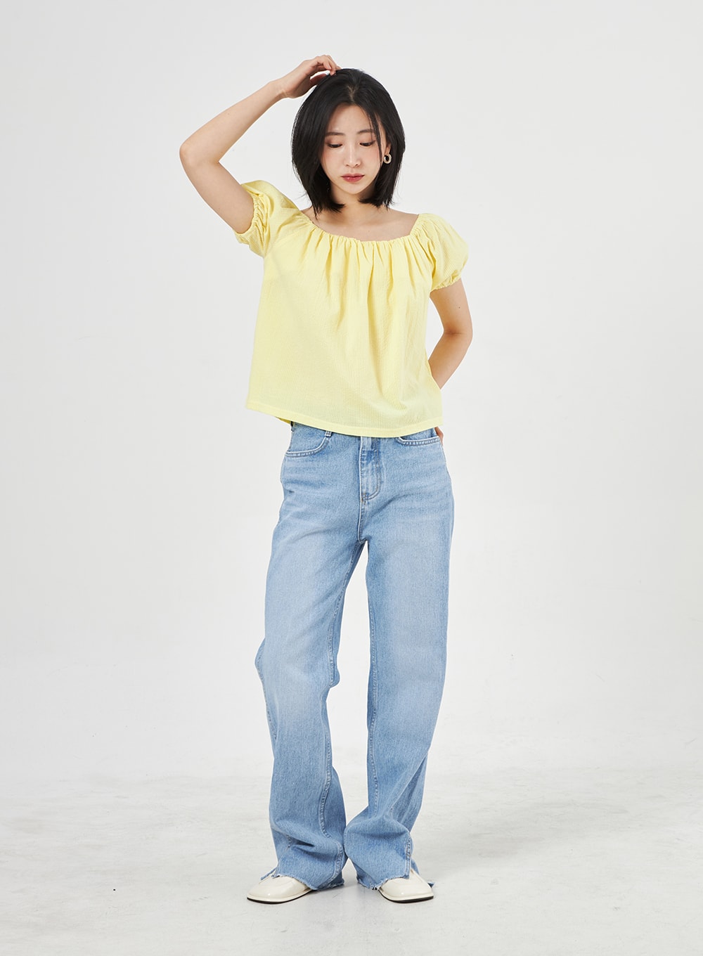 Light Wash Jeans OA310 in light blue, front full-length editorial shot on model with hand in hair, wide-leg washed cotton denim with side slit hem detail, styled with yellow top.