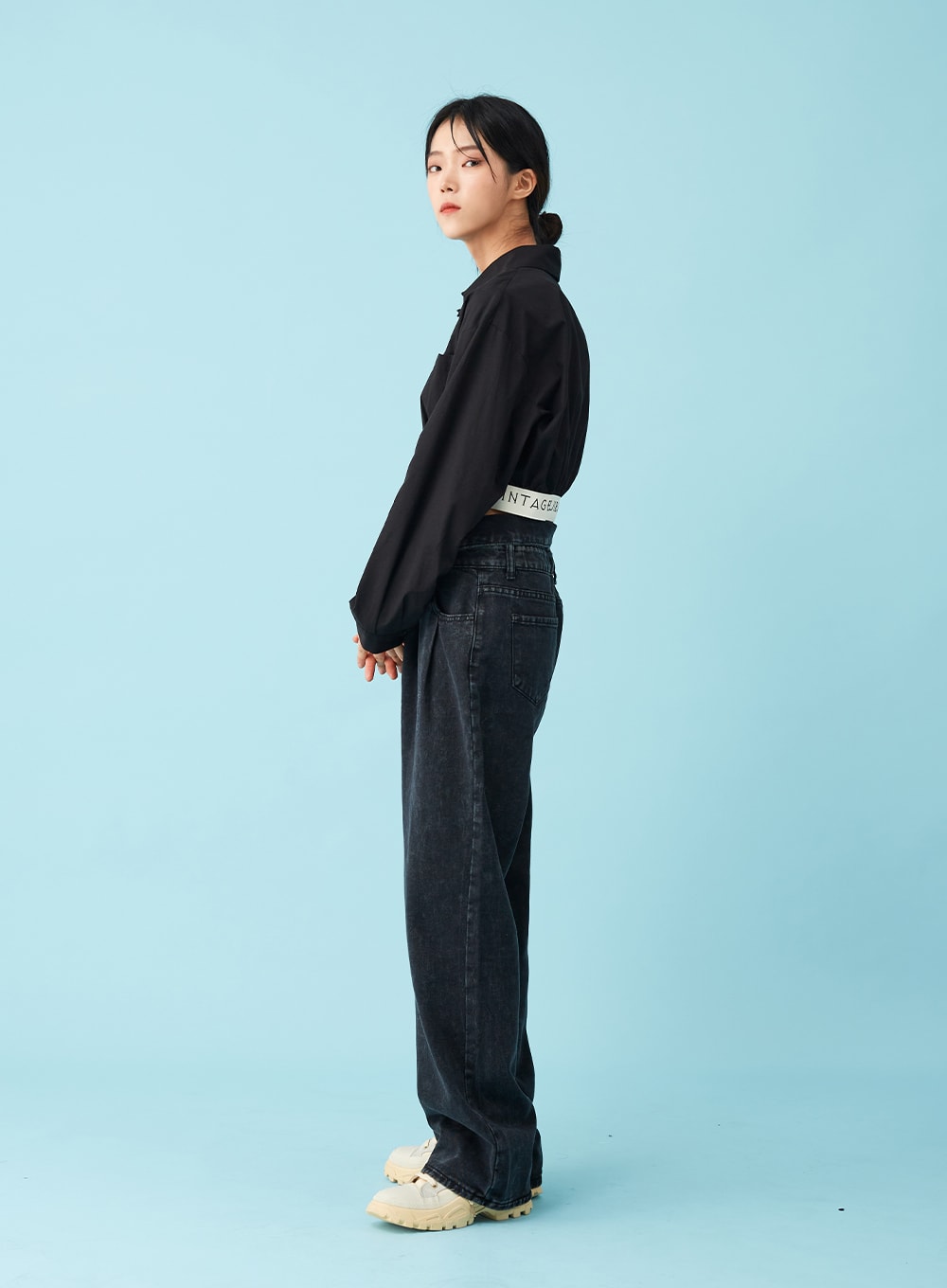 Four Buttoned Open Black Jeans CU8 in washed black, side profile full-length on model, wide-leg cotton denim with straight fall, open folded waistband and logo belt at side, black crop shirt.