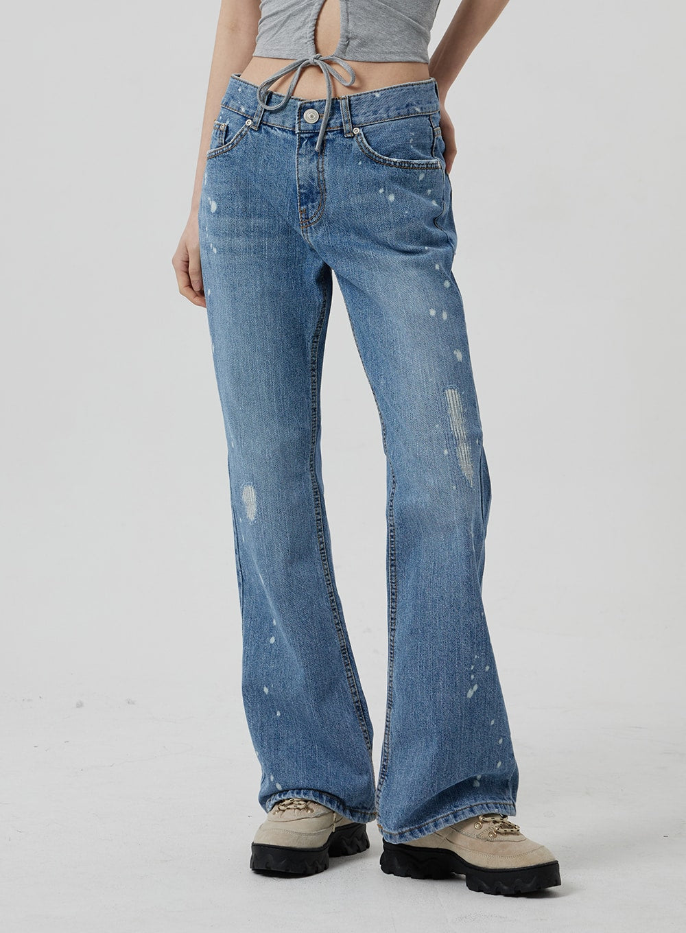 Low Rise Bootcut Jeans CF309 in blue denim, front side-angle close-up on model from hip to ankle, low-rise waistband with visible stitching, paint-splatter and abrasion detailing, gradual bootcut flare.