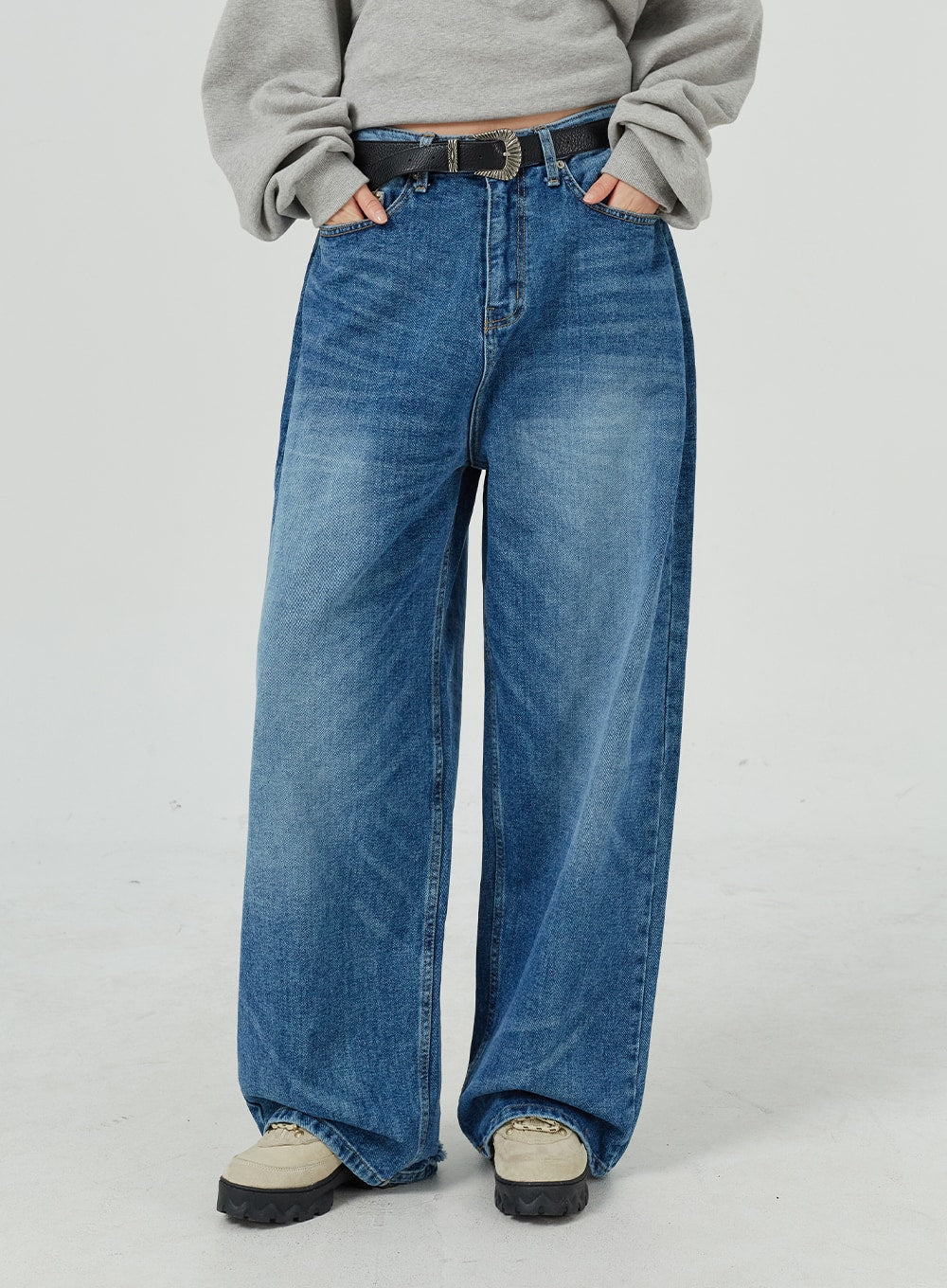 Oversized Jeans Unisex CM321 in blue, waist-to-ankle front mid-shot hands in pockets, wide-leg denim with heavy washed fading and western belt accent.