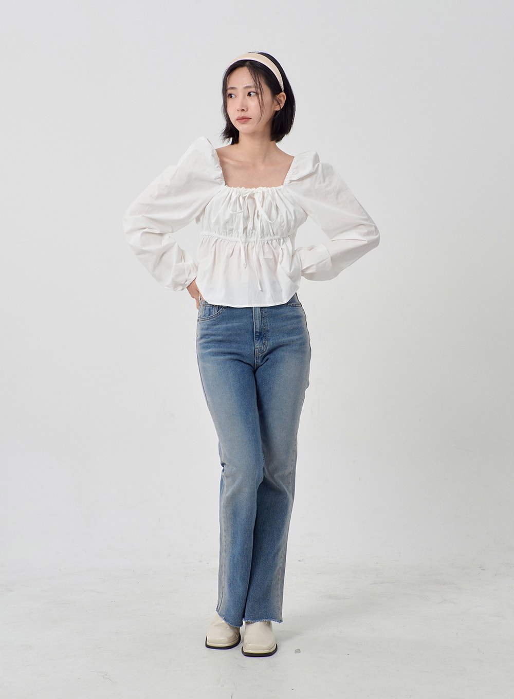 Light Washed Bootcut Jeans OD27 in light blue, front full-body shot on model with hands on hips, slim-fit washed cotton denim, bootcut silhouette with raw hem, styled with white puff-sleeve top.