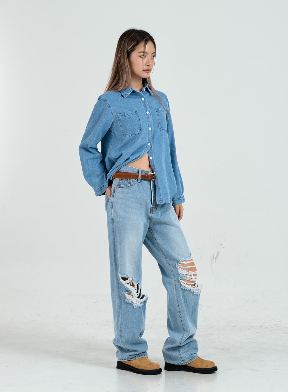 Ripped Maxi Denim Pants Unisex CO14 in light blue, three-quarter side view on model, wide-fit destroyed denim with frayed knee rips, styled with denim shirt and brown leather belt.