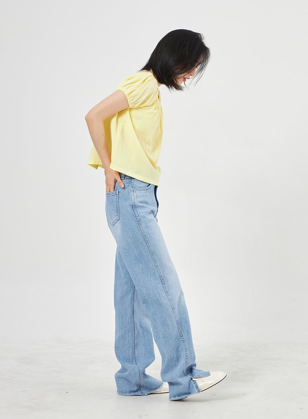 Light Wash Jeans OA310 in light blue, side shot on model leaning forward, wide-fit washed denim highlighting leg width and slit hem, paired with yellow puff-sleeve top.