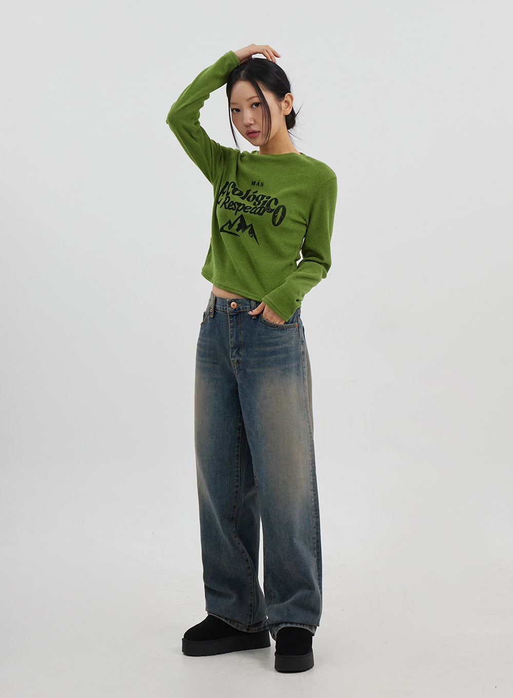 Mid-Rise Baggy Jeans Unisex CJ330 in vintage blue, full-body front view on model with hand raised, wide-fit faded denim showing baggy silhouette, styled with green graphic knit.