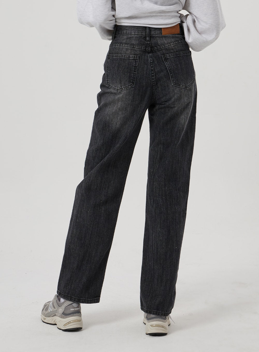 Wide Straight Leg Jeans BF310 in washed black, back close-up on model, showing dual back pockets, brown leather patch, and wide straight leg hem, paired with grey sneakers.