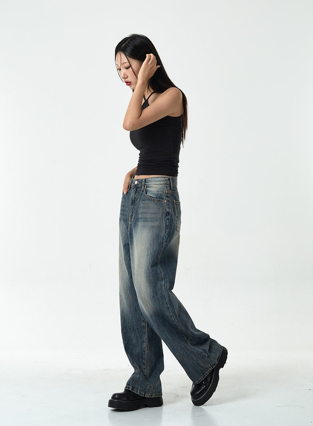 Washed Denim Pants CG10 in dark blue, full side view on model in walking pose, wide-leg washed denim with vintage fading, silhouette flowing from hip to floor, paired with black halter top.