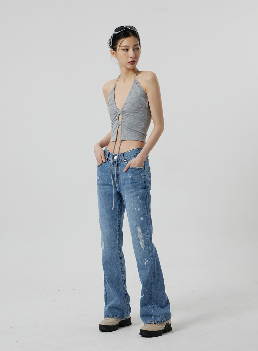 Low Rise Bootcut Jeans CF309 in blue denim, full-length front view on model, hands in pockets, slight three-quarter angle, paint-splatter distressing on bootcut leg, paired with grey ruched halter crop top.