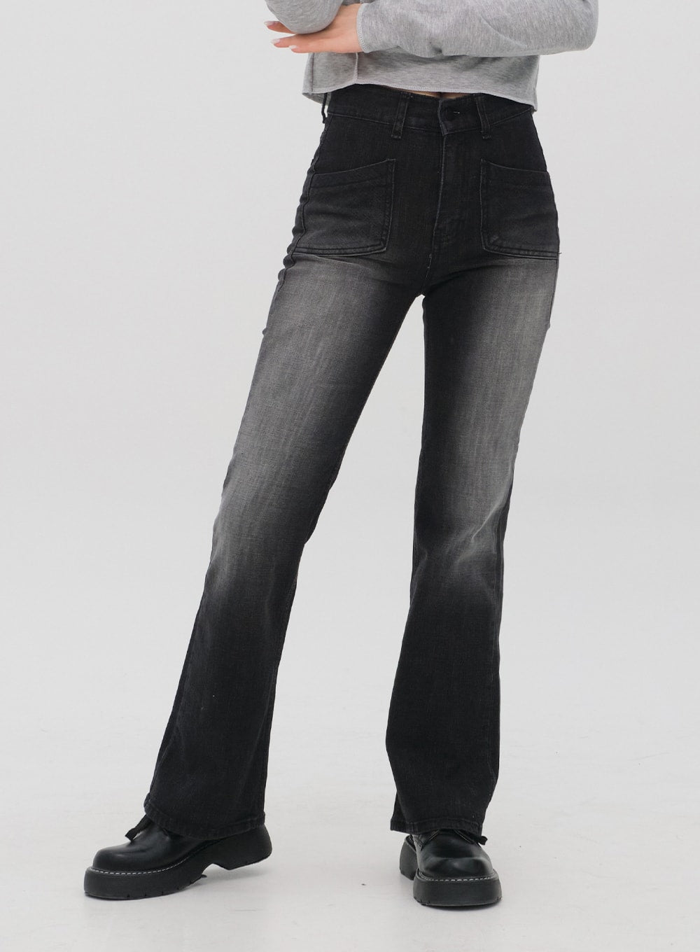 Bootcut Jeans M4 in black gradation wash, front lower-body close-up on model, patch front pockets, gradation fade from dark at waist to grey at knee, long bootcut hem.