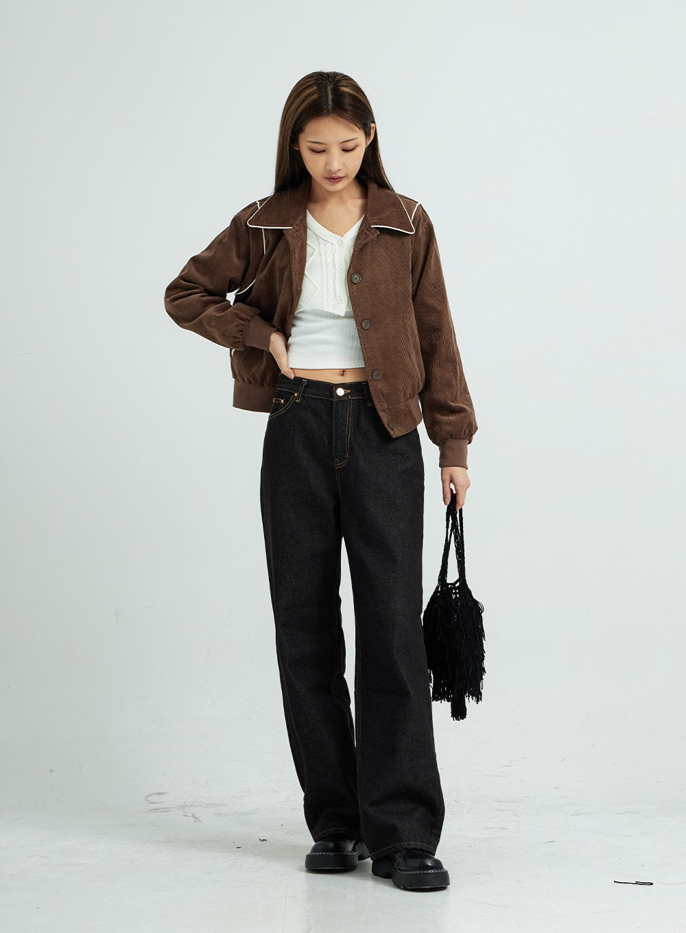 Pepe Wide Pants CS15 in black, full-length three-quarter view on model looking down, wide-fit cotton denim with contrast stitching, layered with brown corduroy jacket and black fringe bag.