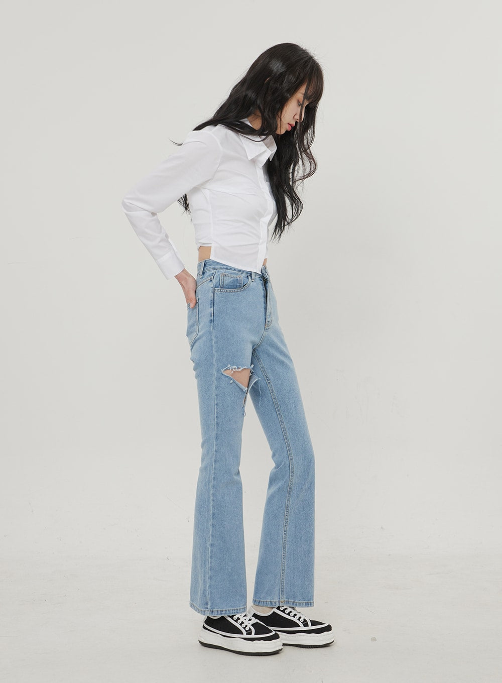 Ripped Bootcut Jeans BF306 in light blue, side view on model looking down, destroyed thigh rip from side angle, high-rise waist and slight bootcut hem, with white crop shirt.