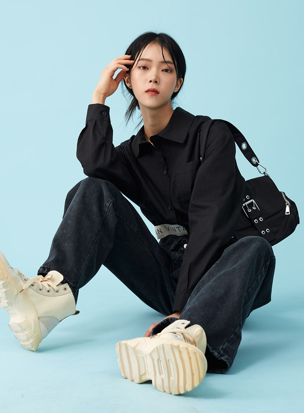 Four Buttoned Open Black Jeans CU8 in washed black, editorial seated pose on model, wide-leg denim spread on floor, open waistband with logo belt visible, black crop shirt and crossbody bag.