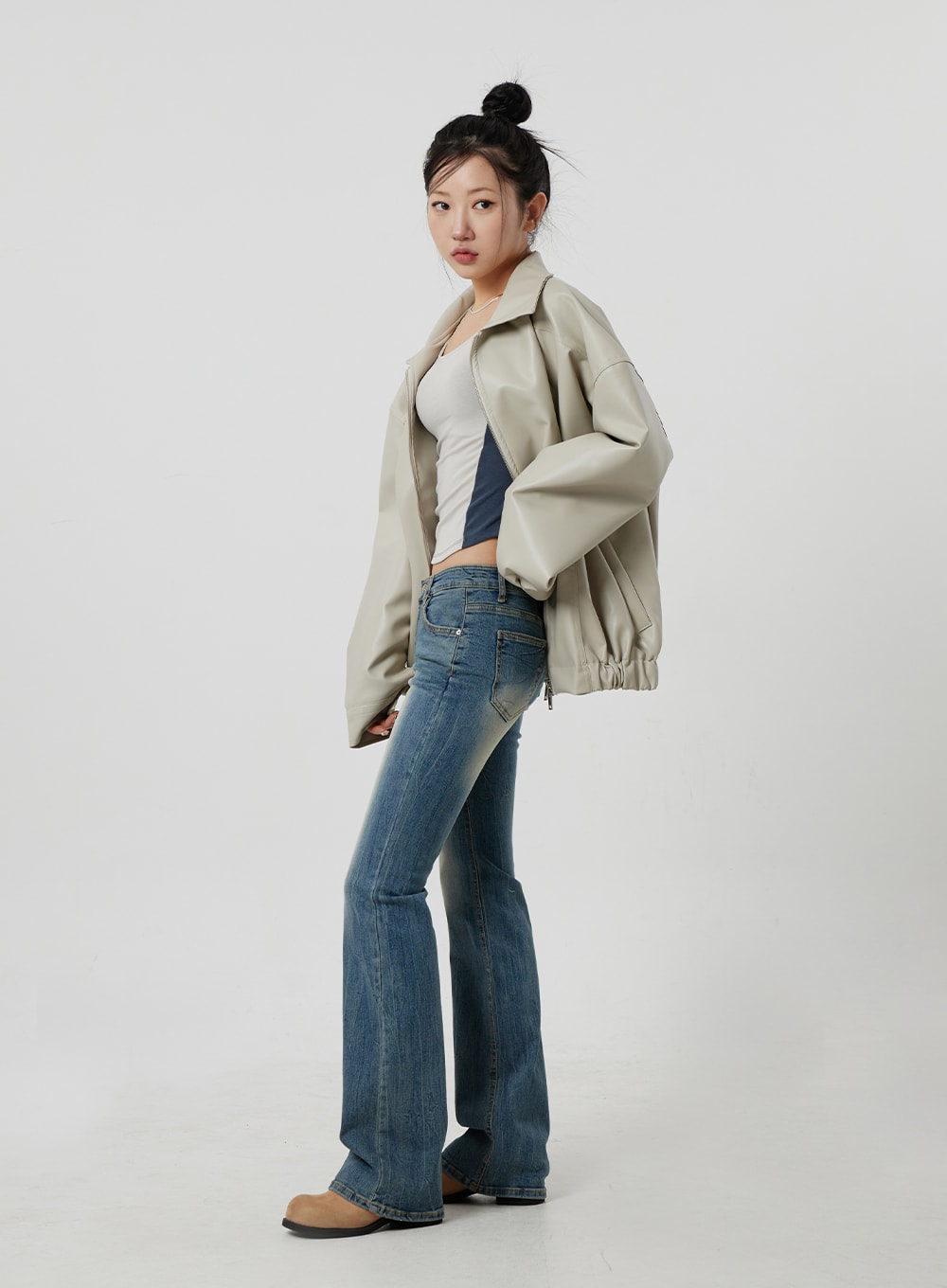 Low Rise Bootcut Jeans CF302 in blue, full-length side-angle shot on model, low waist slim fit with bootcut hem, faded blue denim, layered with oversized beige leather jacket.