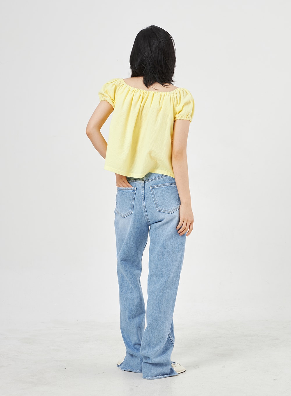 Light Wash Jeans OA310 in light blue, back full-length shot on model, wide-leg washed denim with stitched back pockets and frayed side slit hem, worn with yellow top.