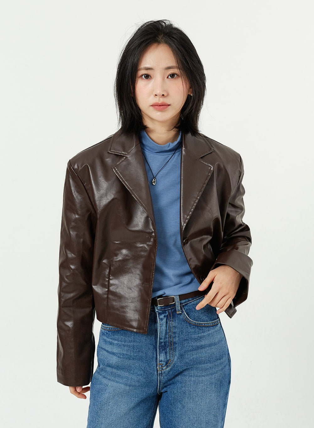 Side Slit Jeans OM308 in mid blue, upper-body front close-up on model, high-rise waistband and belt detail visible, paired with brown leather jacket and blue turtleneck.