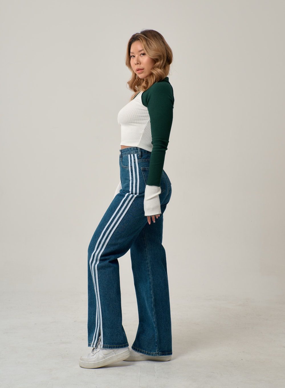 Side Stripes Straight Leg Jeans IN22 in mid blue, side profile shot on model looking over shoulder, three white stripes running full outer-leg length on wide-fit straight denim, cut-out hem at ankle.