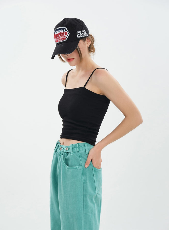 Basic Cropped Cami Top CA20 in black, side view on model looking down, thin straps and fitted cropped silhouette, paired with teal wide-leg jeans and graphic cap.