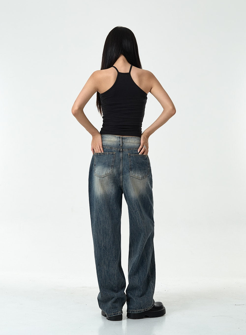 Washed Denim Pants CG10 in dark blue, full back view on model, wide-leg washed cotton denim with faded crinkle finish, two back pockets, paired with black halter top and chunky loafers.