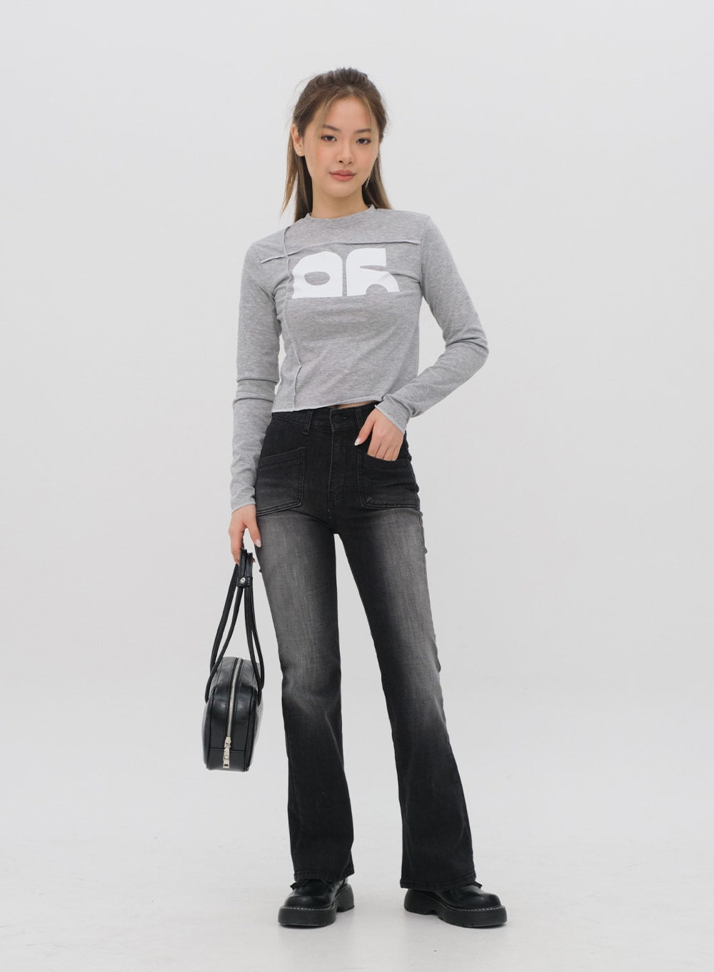 Bootcut Jeans M4 in black gradation wash, full-body front shot on model holding black bag, high-waist patch pockets, cotton bootcut denim, gradation fade, long length.