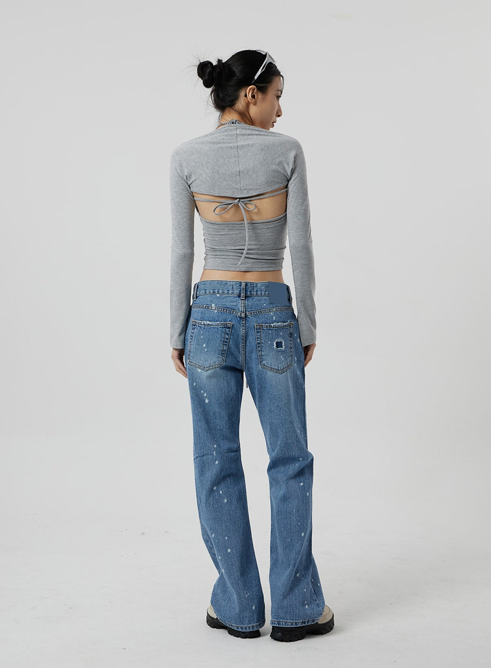 Low Rise Bootcut Jeans CF309 in blue denim, full-length back view on model, rear pockets with patch label, paint-splatter distressing throughout, bootcut hem, paired with grey long-sleeve backless halter crop top.