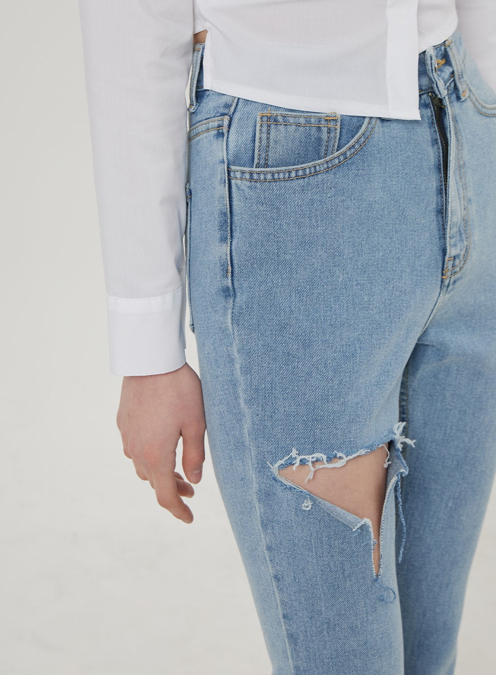 Ripped Bootcut Jeans BF306 in light blue, close-up detail of destroyed thigh rip, frayed raw-edge cutout with cotton threads visible, high-rise front panel and pocket stitching shown.