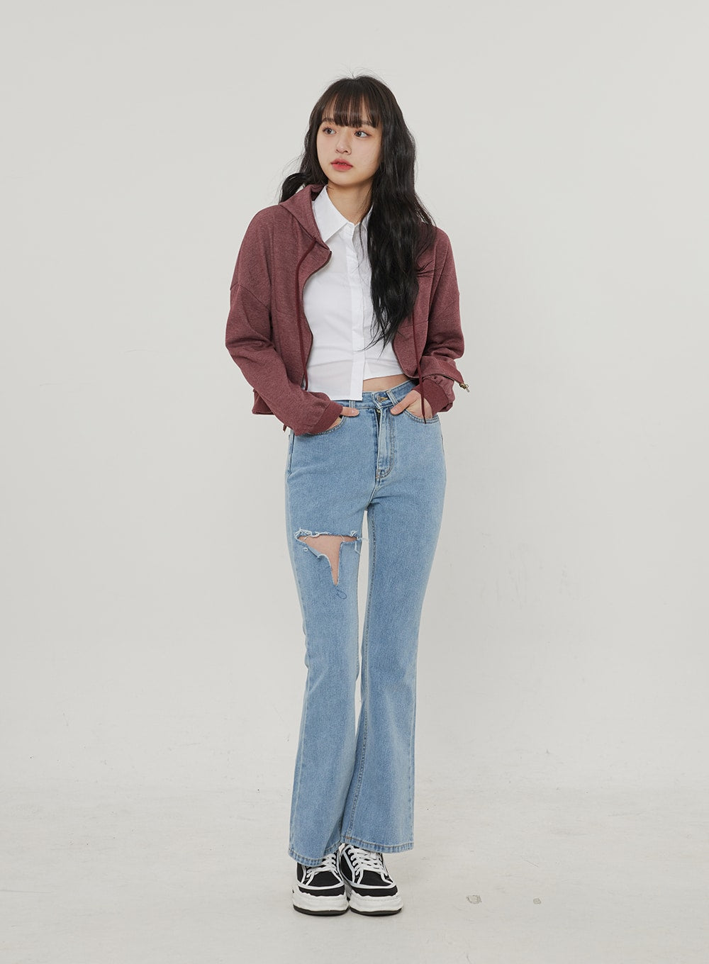 Ripped Bootcut Jeans BF306 in light blue, front full-body on model, destroyed thigh cutout and bootcut silhouette, layered styling with white crop shirt and burgundy zip-up jacket.