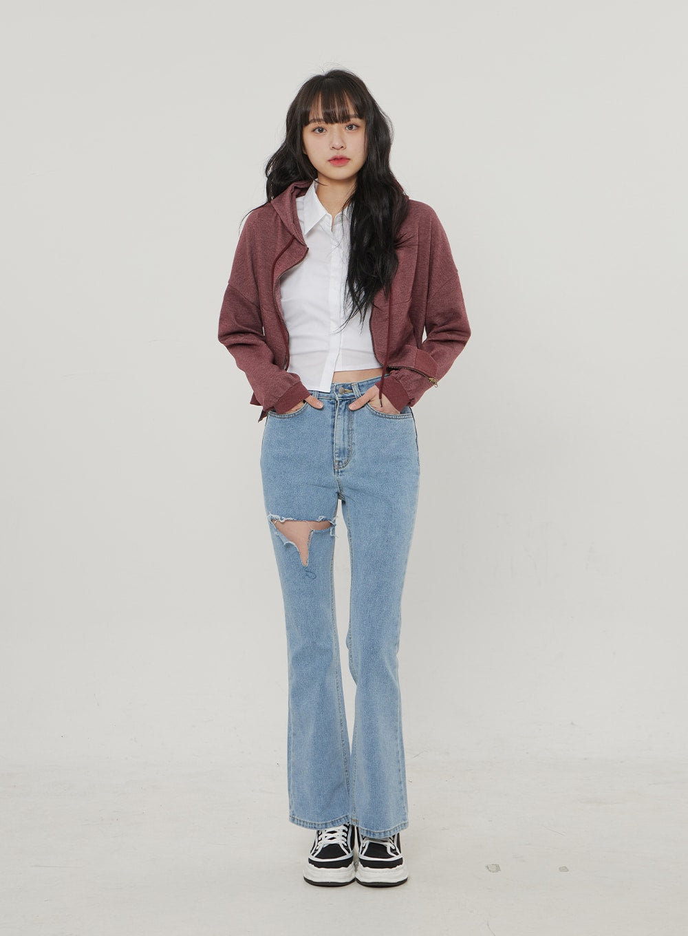 Ripped Bootcut Jeans BF306 in light blue, front full-body on model hands in pockets, slim high-rise fit with large ripped cutout, styled with white crop shirt and burgundy jacket.