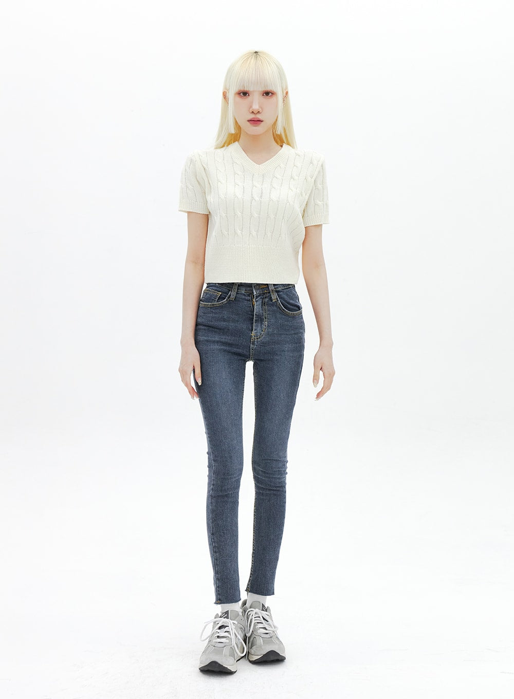 Skinny Ankle Jeans BA321 in dark blue denim, full-body front shot on model standing straight, high-rise skinny silhouette, styled with cream cable-knit crop top and grey sneakers.