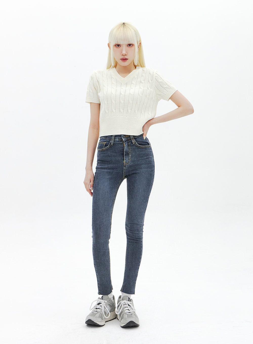 Skinny Ankle Jeans BA321 in dark blue denim, full-body front shot on model with hand on hip, high-rise waist, slim ankle length, paired with cream cable-knit crop top and sneakers.