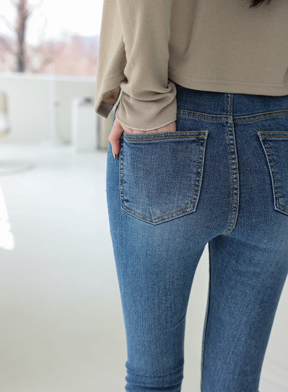 Double Button Raw Hem Skinny Jeans IA11 in mid blue denim, back close-up of hip area, showing back patch pocket with contrast topstitching, faded wash texture, and body-hugging skinny fit.