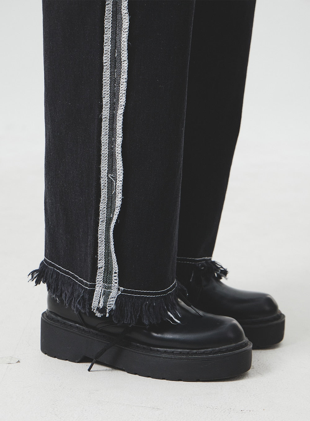 Stitch Detail Jeans BA307 in black, macro close-up of hem area on model, showing exposed overlocked side stitch stripe and dense raw fringe hem detail at ankle.
