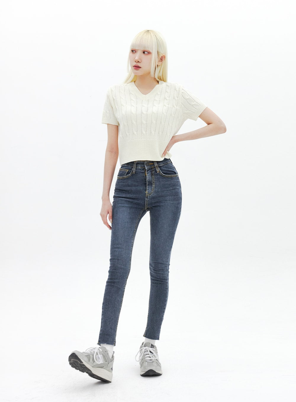 LEWKIN Skinny Ankle Jeans BA321 in dark blue denim, full-body angled shot on model, high-rise skinny fit with gold-tone stitching, paired with cream cable-knit crop top and grey sneakers.