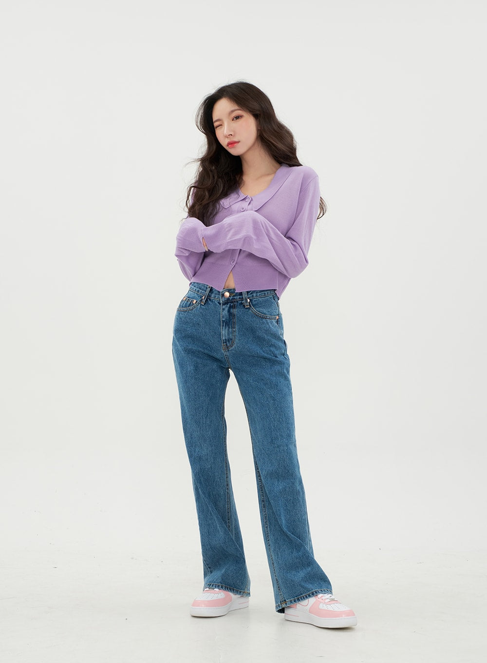 Semi Wide Jeans BM21 in mid-blue denim, front view on model with arms crossed, wide-leg cotton denim showing high-rise waistband and zip-up closure, paired with purple knit top.