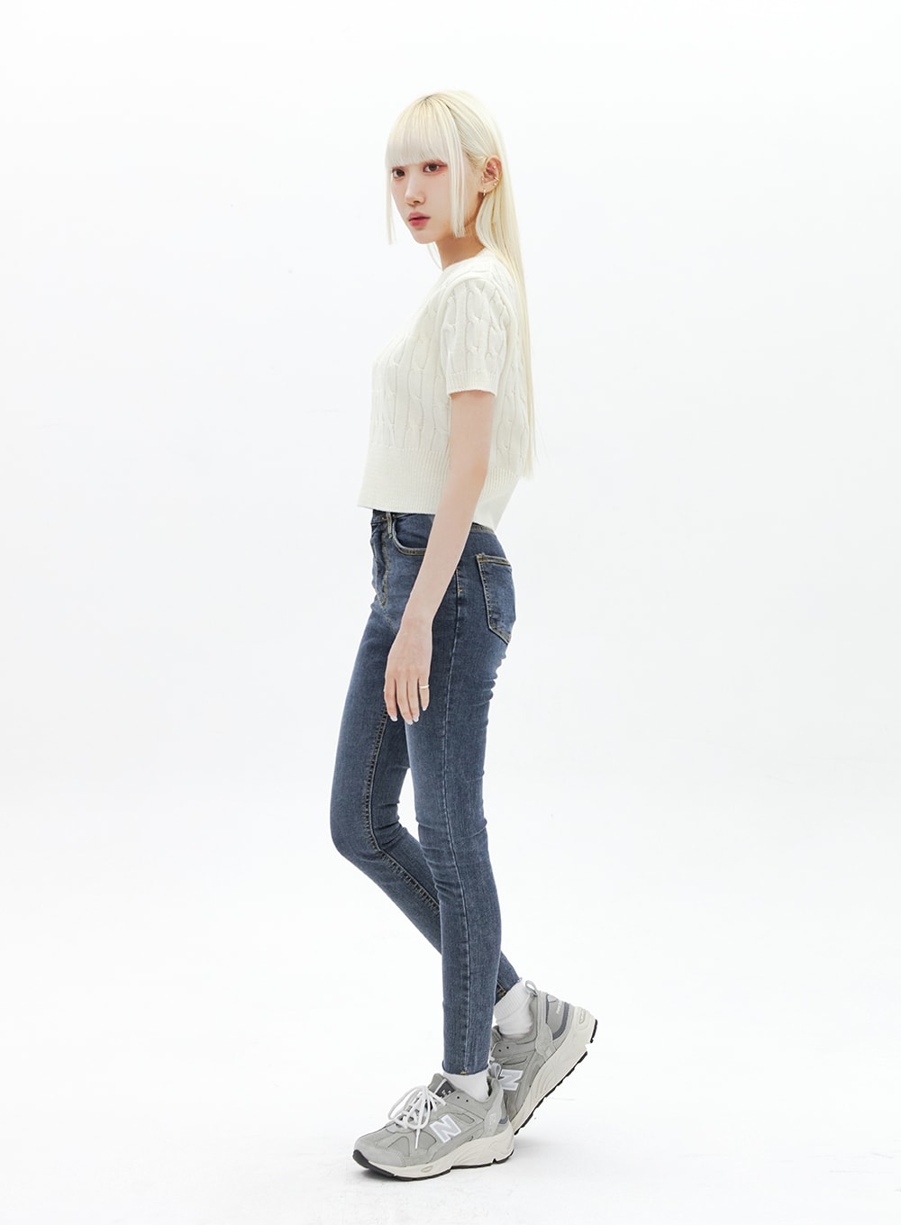 Skinny Ankle Jeans BA321 in dark blue denim, side profile full-body shot on model, high-rise skinny fit with tapered ankle, paired with cream cable-knit crop and grey sneakers.