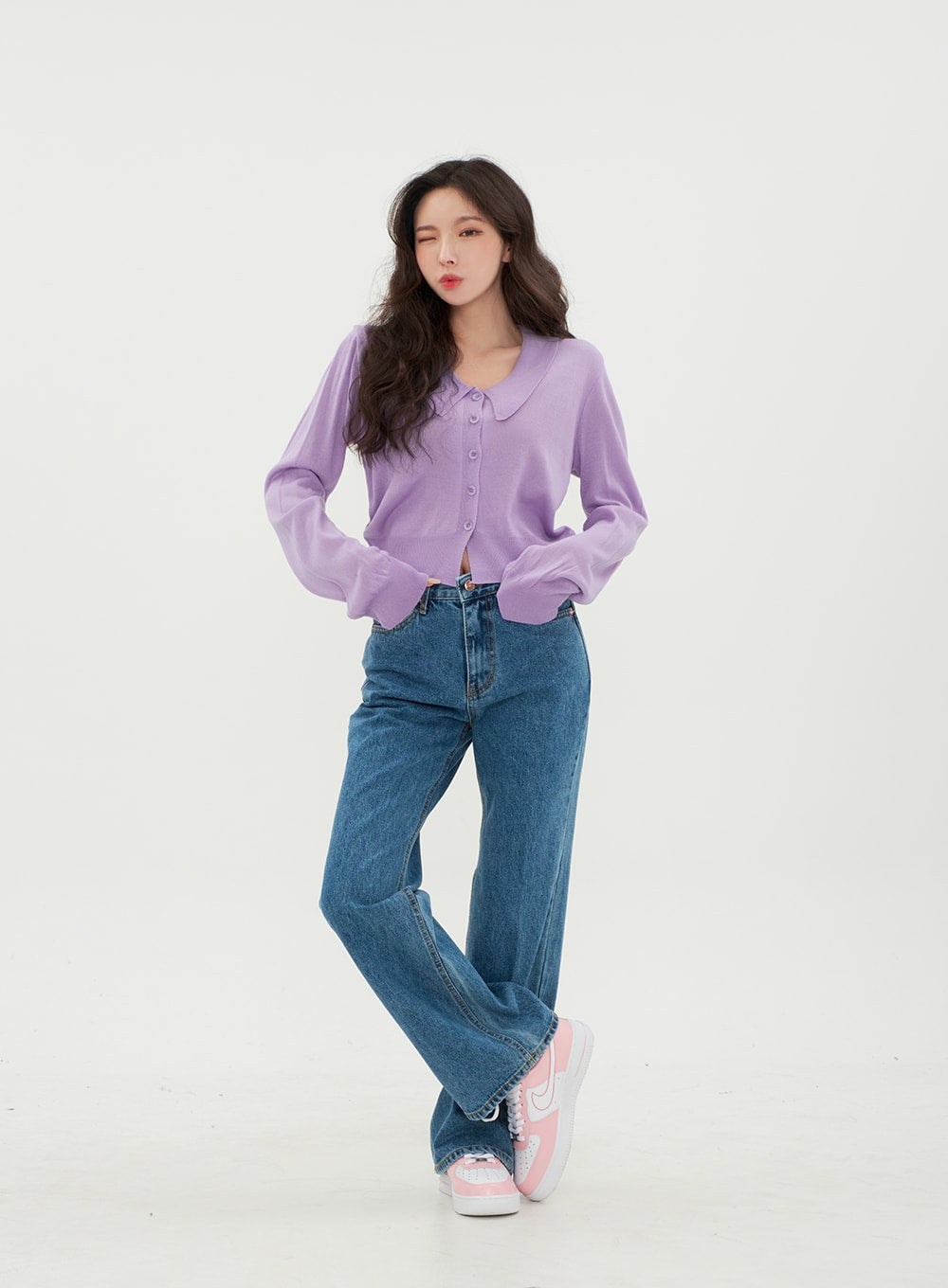 Semi Wide Jeans BM21 in mid-blue denim, front relaxed cross-legged pose on model, long wide-fit solid cotton denim with front pockets, styled with cropped lavender cardigan and sneakers.