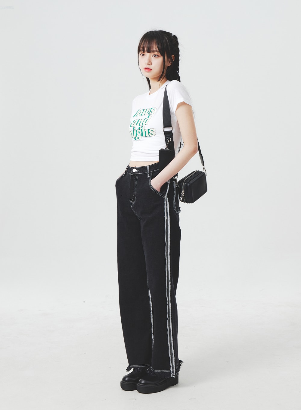 LEWKIN Stitch Detail Jeans BA307 in black, angled full-length shot on model, wide-fit cotton denim with contrast side stitch stripe and frayed hem, styled with white crop tee and black crossbody bag.