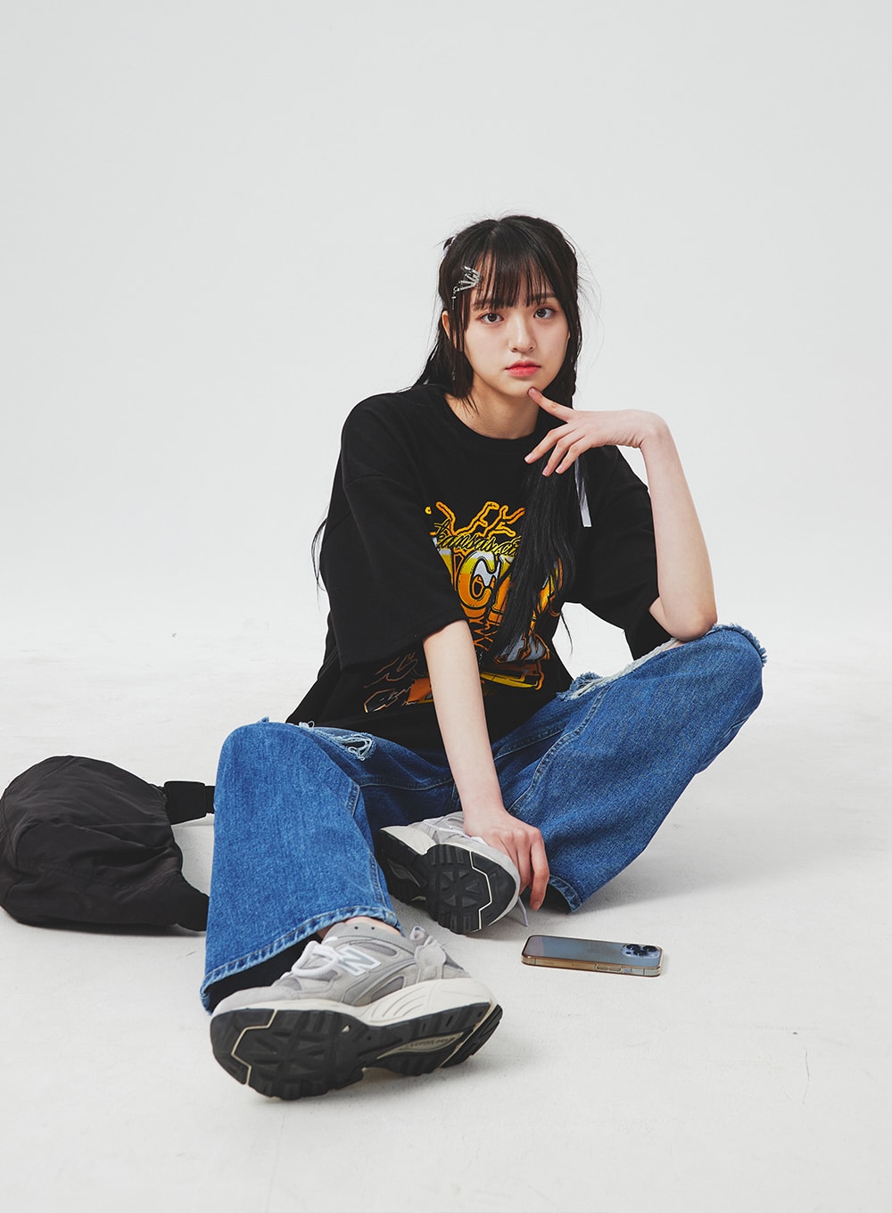 Ripped Knee Blue Jeans BA307 in blue, seated floor-level lifestyle shot on model, wide-fit destroyed knee denim with faded wash, styled with black graphic tee and chunky sneakers.