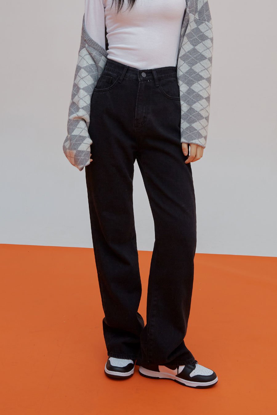 LEWKIN Straight Leg Pants J23 in black, front cropped view on model, high-waist cotton straight-fit denim, front pockets visible, styled with argyle cardigan and sneakers.