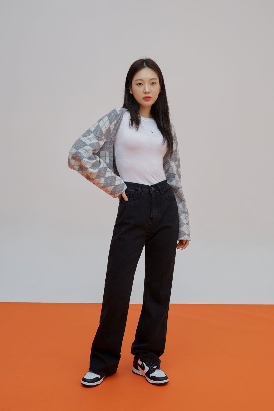 Straight Leg Pants J23 in black, full-length front shot on model, long straight cotton denim, high waist, paired with white tee, argyle cardigan, and Jordan sneakers.