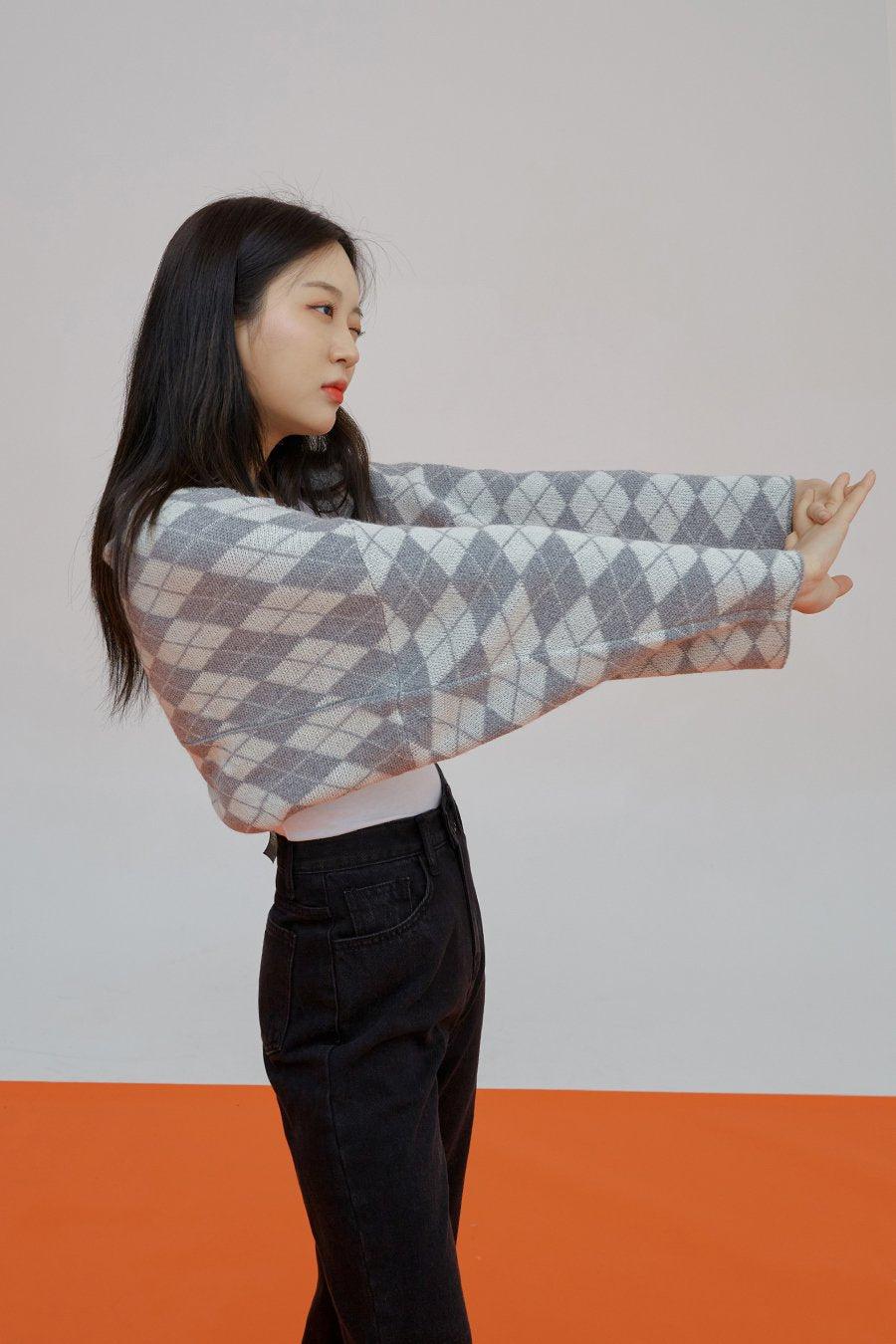 Straight Leg Pants J23 in black, upper side close-up on model, high-waist cotton denim with front pocket, model posing with arms extended, argyle cardigan overlay.